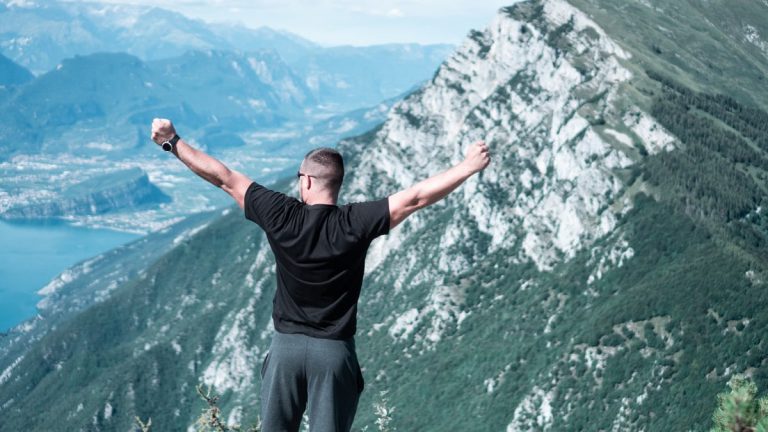 Man standing with arms raised in celebration overlooking a breathtaking mountain landscape.